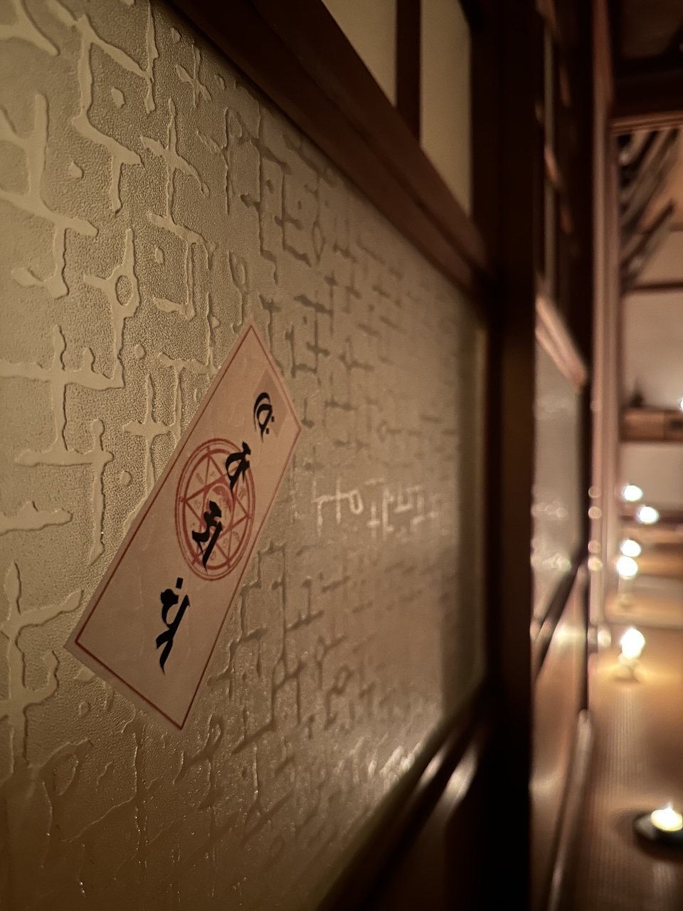 古民家の硝子に貼られた護符と、奥に続くロウソクの灯りが演出するTHE KAIDAN 第2夜の会場雰囲気