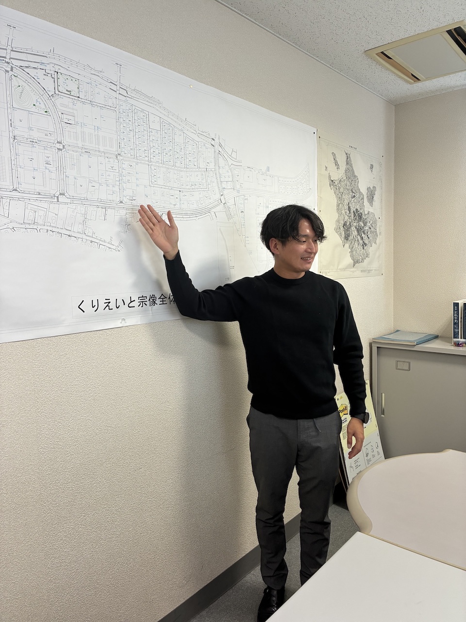 宗像市のエリアマップを前に不動産活用やまちづくり構想を説明するスタッフ。家を売るだけでなく地域の未来に関わる不動産の仕事