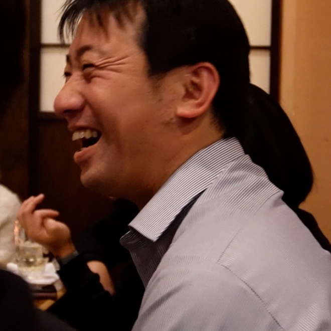 飲食店の席で大きく笑っている男性。リラックスした雰囲気で、周囲と楽しく会話している様子