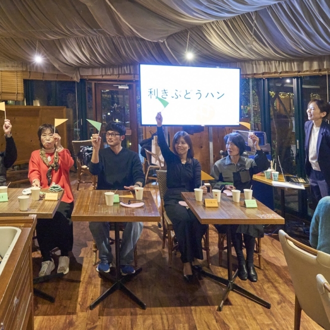 忘年会の格付けゲームで参加者が札を掲げ、会場が盛り上がっている様子