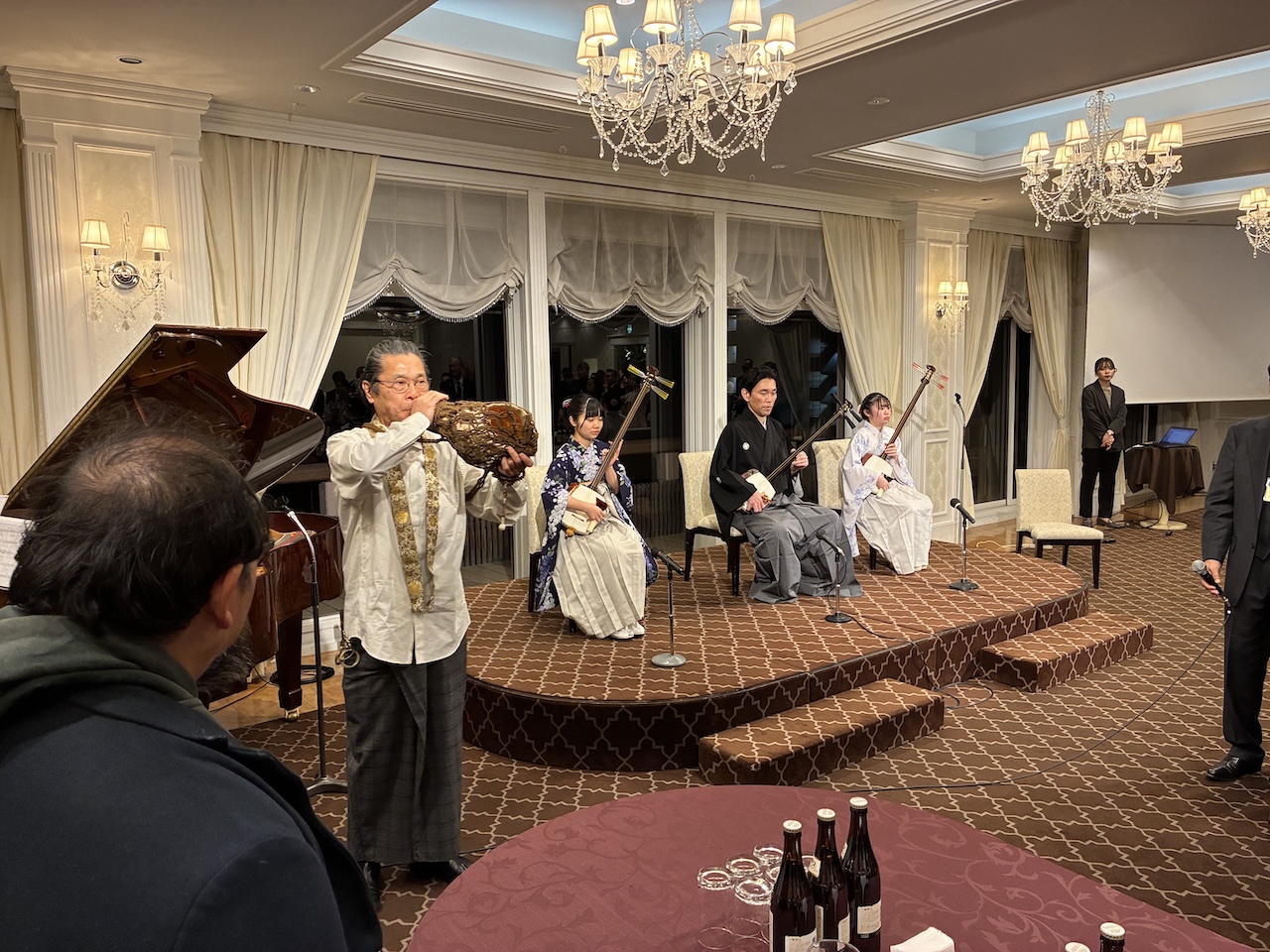 室内ステージで、ほら貝の演奏者と津軽三味線奏者が新年会の演奏を行う様子