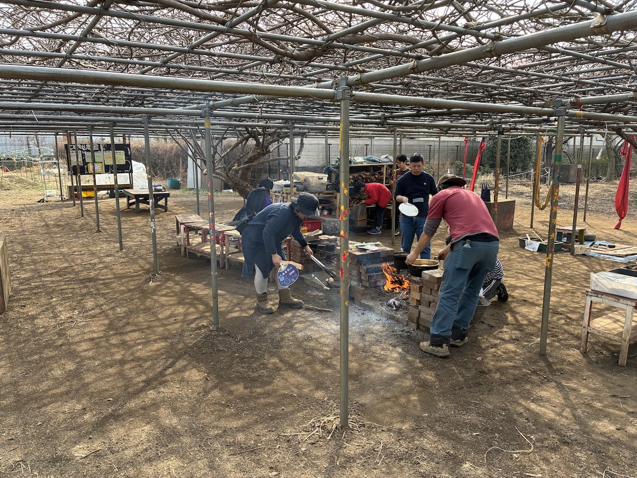 屋外の公園で、焚き火台の周りに人が集まり、火を囲んで暖を取っている様子