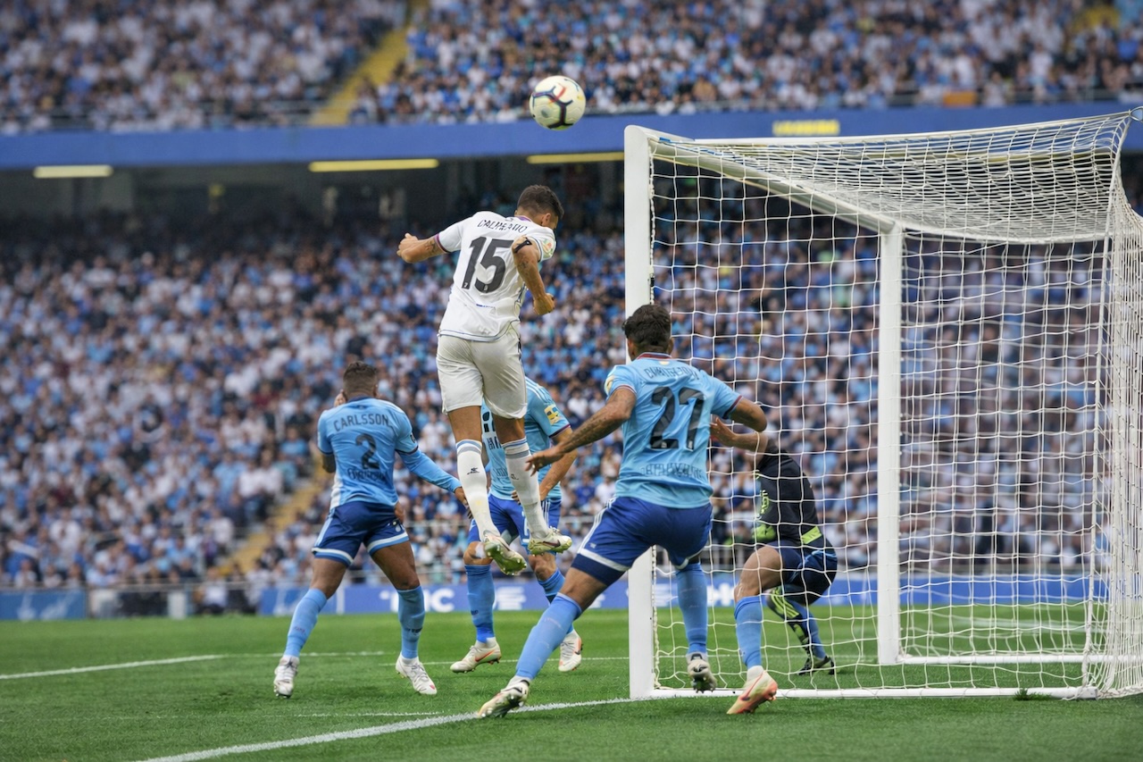 ゴール前のセットプレーで、白いユニフォームの選手がヘディングでボールを合わせる瞬間