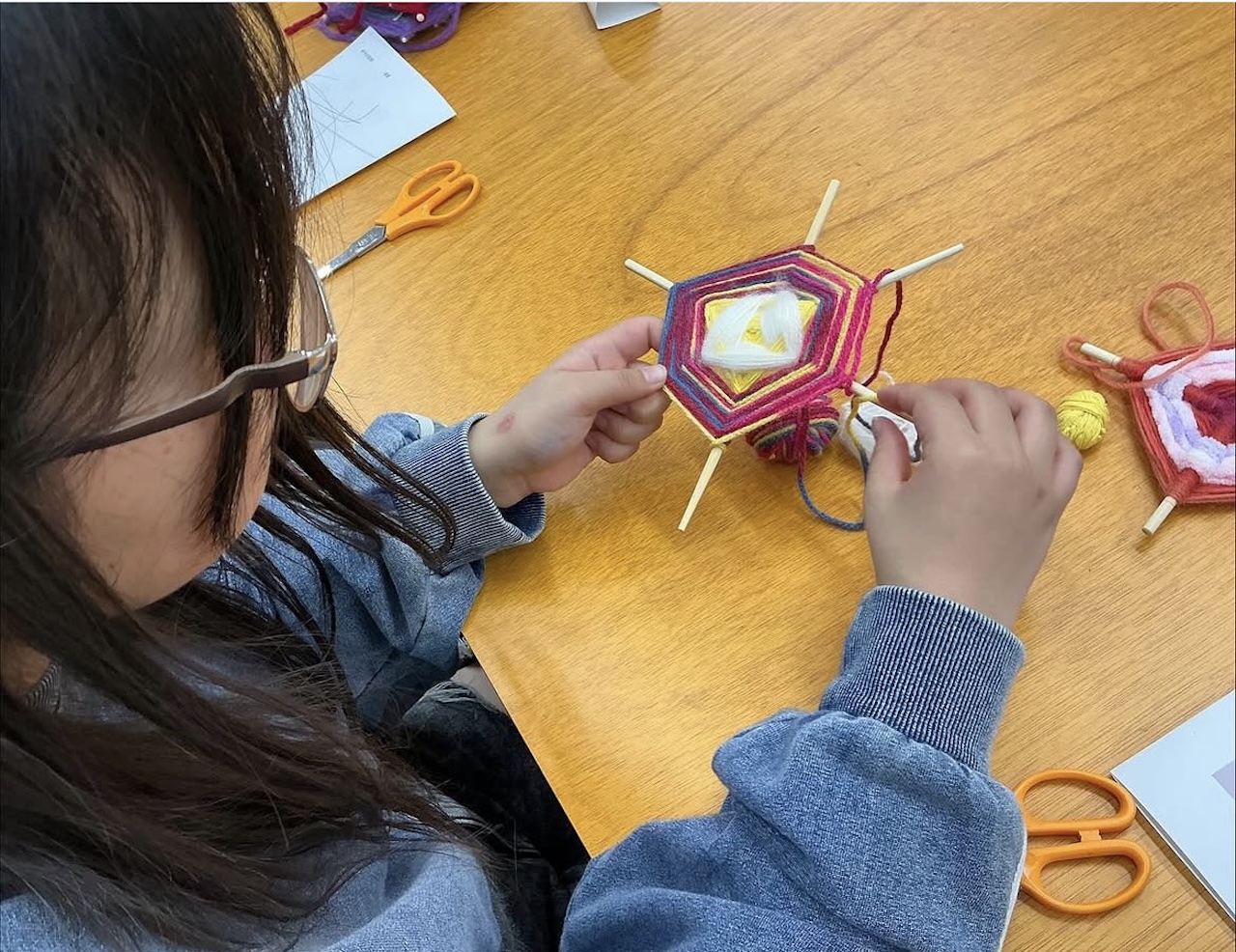 糸を重ねながら色彩豊かなお守りづくりに取り組む中学生の手元