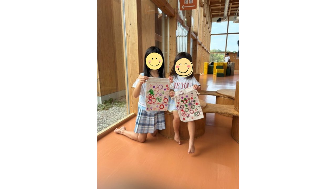 木造施設内で手作りの布バッグを見せる2人の子どもたち