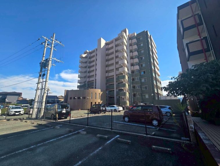 青空の下に建つ10階建てマンションの外観と駐車場