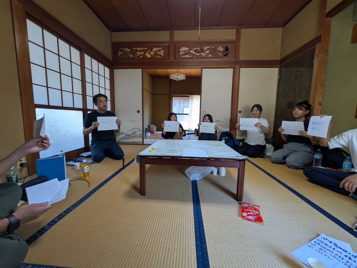 畳の和室でアイデアを書いた紙を掲げるスタッフたちの会議風景
