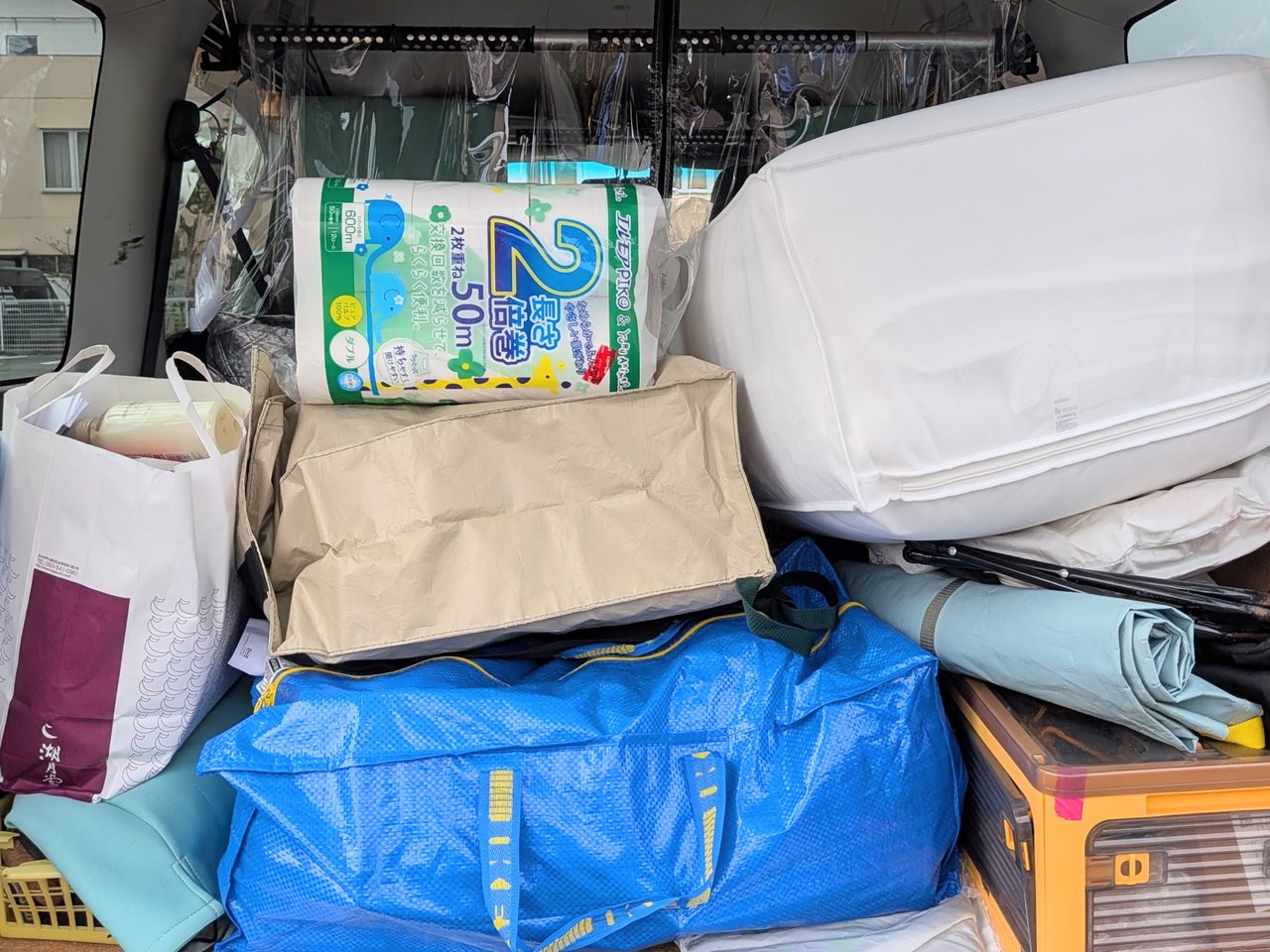 車の荷台に段ボールやIKEAバッグ、トイレットペーパーなどの荷物がぎっしり積まれている