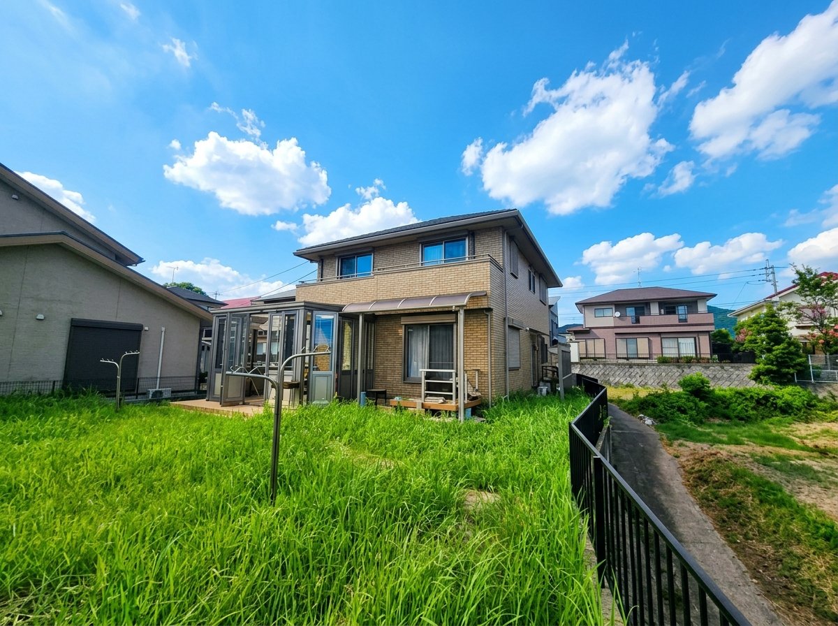 青空と広い芝生の庭が広がる2階建て戸建住宅、サンルーム付き