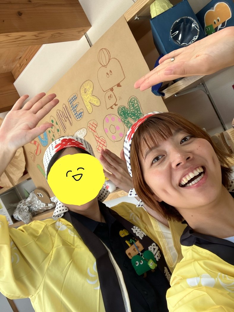 黄色い法被を着たスタッフ2人がSUMMERの手作り看板の前で笑顔でポーズ
