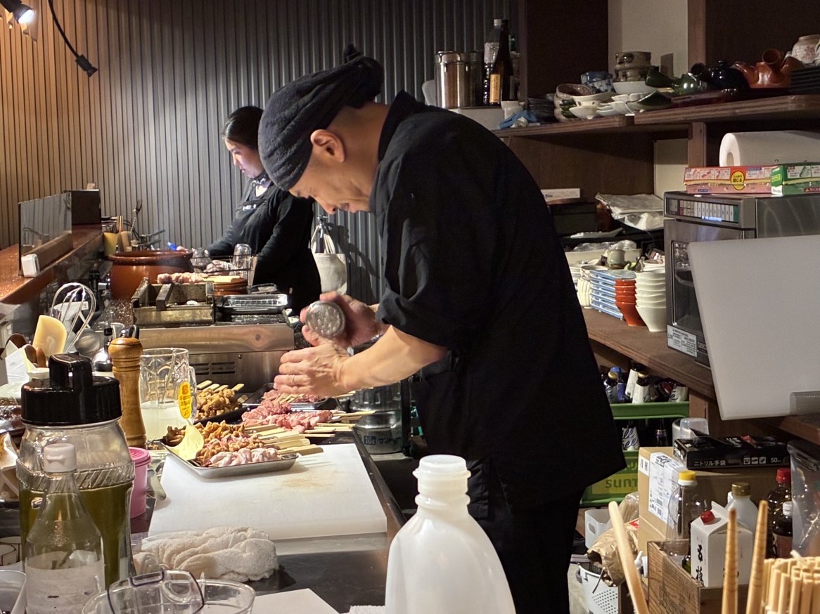 下関市のもつ焼き屋「幸」の厨房で黒い服を着たスタッフが串を仕込む様子