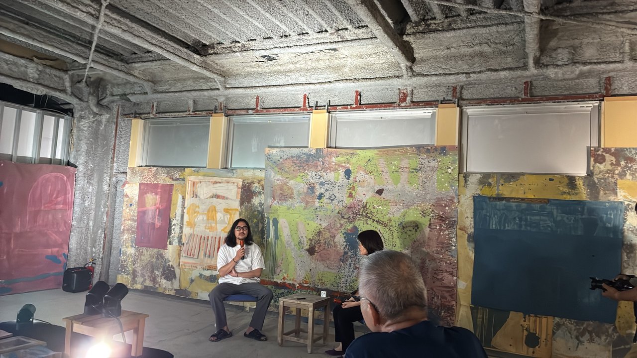 赤間駅で開催されたパンクス三女神展のアーティストトーク風景。大型の抽象画を背景にアーティストがマイクを持って語る